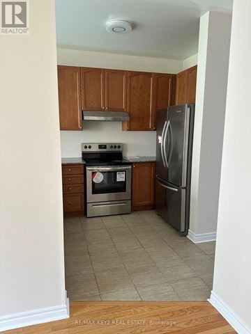 Pickering (Duffin Heights) apartment for rent - A kitchen with a stove top oven, refrigerator, and wooden cabinets.