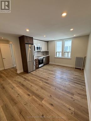 Toronto (Forest Hill South) house for rent - A spacious room with wooden flooring and a kitchen area with stainless steel appliances.
