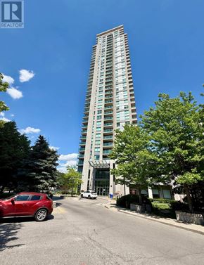 Toronto (Bendale) condo for rent - A tall building with a glass facade stands next to a street with cars and trees.
