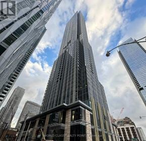 Toronto (Annex) condo for rent - A tall, modern glass skyscraper stands in a cityscape.