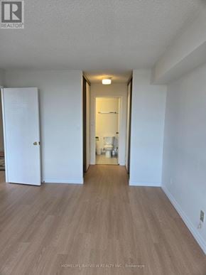 Toronto (Steeles) condo for rent - A room with wooden flooring and white walls, with a door on the left and a hallway on the right.
