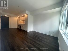 Toronto (North St. James Town) condo for rent - A spacious room with wooden flooring and a kitchenette in the background.