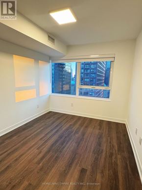 Toronto (North St. James Town) condo for rent - A room with wooden flooring and a window showing a city view.