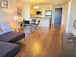 Markham (Unionville) condo for rent - A living room with a grey couch and a kitchen area in the background.