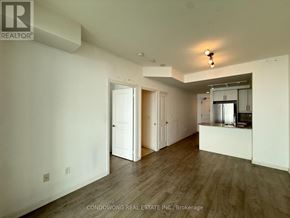Toronto (Niagara) condo for rent - A spacious room with wood flooring and white walls, with a kitchenette visible in the background.