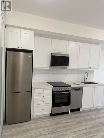 Clarington (Bowmanville) condo for rent - A kitchen with white cabinets and a stainless steel refrigerator.