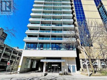 Toronto (University) condo for rent - A tall building with a blue stripe on the side and a parking garage in front.