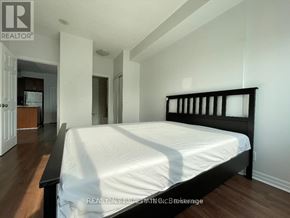 Mississauga (City Centre) condo for rent - A bedroom with a large bed and a kitchen area in the background.