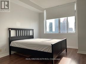 Mississauga (City Centre) condo for rent - A bedroom with a large bed and a window overlooking a city skyline.
