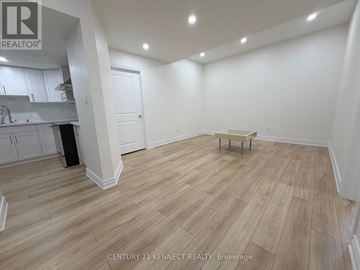 Oakville (Jm Joshua Meadows) apartment for rent - A room with wooden flooring and white walls, with a kitchen area to the left.