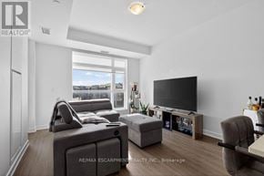 Hamilton (Lakeshore) condo for rent - A living room with a grey couch, a grey ottoman, a black television and a wooden floor.