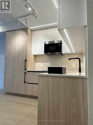 Toronto (Bayview Village) condo for rent - A modern kitchen with wooden cabinets and a microwave oven.
