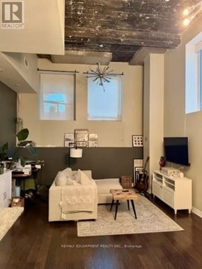 Hamilton (Central) condo for rent - A living room with a white couch and a television on a cabinet.