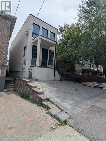 Toronto (Oakwood Village) apartment for rent - A modern house with a flat roof and large windows is surrounded by a brick wall and a paved area.
