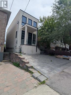 Toronto (Oakwood Village) apartment for rent - A modern house with a flat roof and large windows is surrounded by a brick wall and a paved area.