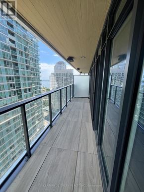 Toronto (Waterfront Communities) condo for rent - A balcony with a glass railing and wooden flooring overlooks a cityscape.