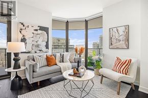 Toronto (Bay Street Corridor) condo for rent - A living room with a grey couch, a white chair, a black floor lamp, and a large window with a view of the city.