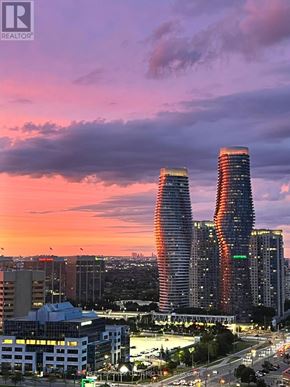 Mississauga (City Centre) condo for rent - Two tall buildings with a lot of windows are lit up at dusk.