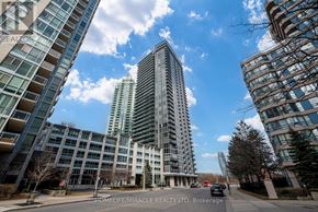 Mississauga (City Centre) condo for rent - A tall residential building stands in the foreground of a street lined with other buildings.