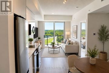 Brantford condo for rent - A well-lit, modern kitchen with a dining table and chairs in the foreground and a balcony with a view of trees in the background.