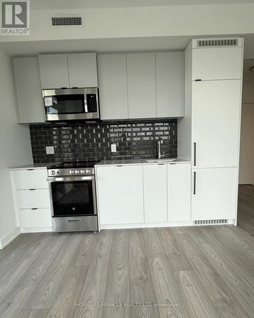 Toronto (South Parkdale) condo for rent - A modern kitchen with white cabinets and a black backsplash.