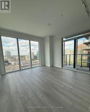 Toronto (South Parkdale) condo for rent - A spacious room with wooden flooring and large windows overlooking a cityscape.