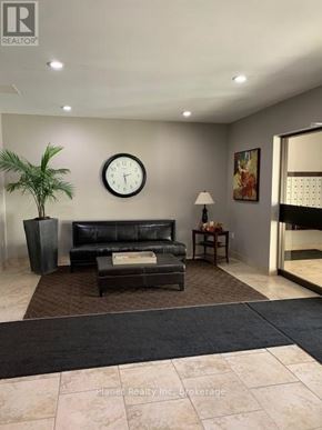 Guelph (Downtown) condo for rent - A living room with a black couch, a plant, a clock, and a lamp.