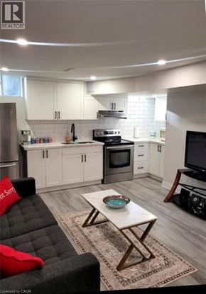 Stoney Creek apartment for rent - A modern kitchen with white cabinets and a black couch with red pillows.