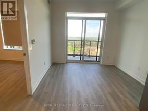 Mississauga (Hurontario) condo for rent - A room with wooden flooring and a large window overlooking a cityscape.