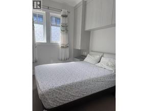 Vancouver apartment for rent - A bed with a white lace bedspread sits in a room with a window and a curtain.