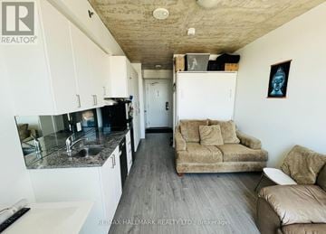 Oshawa (Samac) condo for rent - A living room with a couch, a chair, and a kitchen area with a sink and cabinets.
