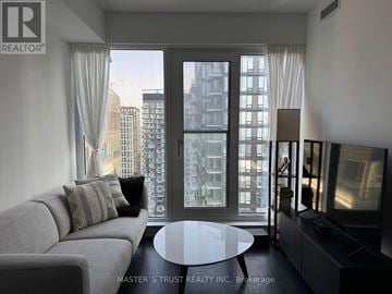Toronto (Waterfront Communities) condo for rent - A living room with a grey couch and a glass table with a city view through the window.
