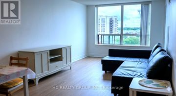 Markham (Commerce Valley) condo for rent - A living room with a black leather couch and a wooden chair.