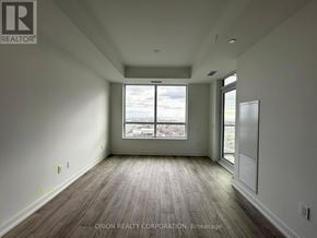Pickering (Bay Ridges) condo for rent - A large, empty room with wooden floors and a view of the city through a large window.