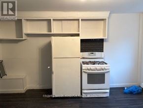 Welland (Welland Downtown) triplex for rent - A white refrigerator and oven in a kitchen with a blue bag on the floor.