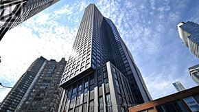 Toronto (Bay Street Corridor) condo for rent - A tall building with a lot of windows stands in front of a blue sky with clouds.