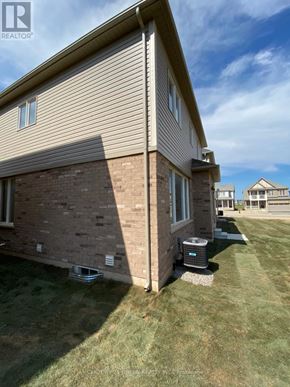 Brantford apartment for rent - A house with a brown siding and a brick wall is shown with a grassy lawn in front.