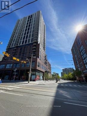 Toronto (Regent Park) condo for rent - A tall building with a glass facade stands next to a street with a traffic light.
