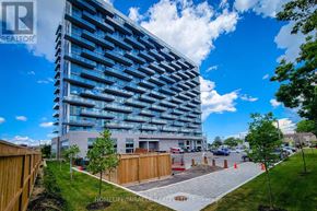 Hamilton (Riverdale) condo for rent - A modern building with a glass facade is surrounded by a wooden fence and trees.