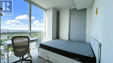 Toronto (Annex) condo for rent - A bedroom with a large bed and a desk with a chair in front of a window overlooking a cityscape.