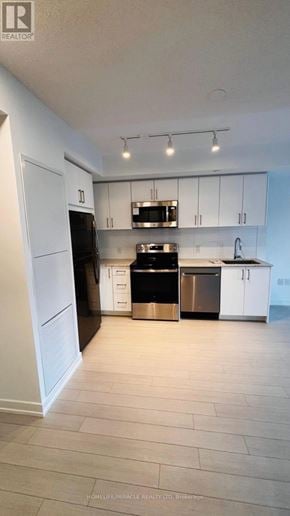 Toronto (Humber Heights) condo for rent - A kitchen with white cabinets and a black fridge.