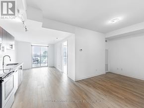 Toronto (Yorkdale-Glen Park) condo for rent - A spacious, well-lit room with wooden flooring and white walls, featuring a kitchen area with stainless steel appliances and a dining table.