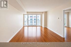 Ottawa condo for rent - A large, empty room with wooden floors and a view of a city skyline through the windows.