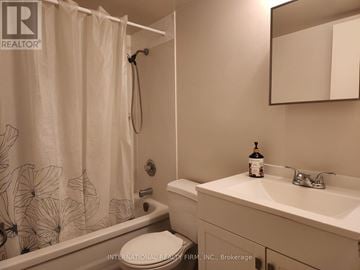 St. Catharines (Glendale/Glenridge) condo for rent - A bathroom with a shower curtain, toilet, sink, and mirror.