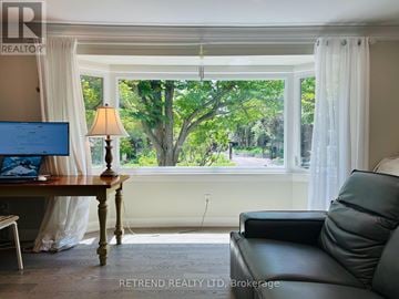 Toronto (Lansing-Westgate) apartment for rent - A living room with a couch, a table with a lamp and a laptop on it, and a window with a view of trees.