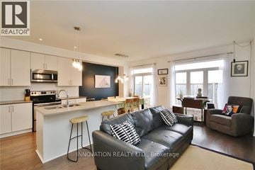 Ottawa townhouse for rent - A modern living room with a black leather couch and a kitchen area with white cabinets.