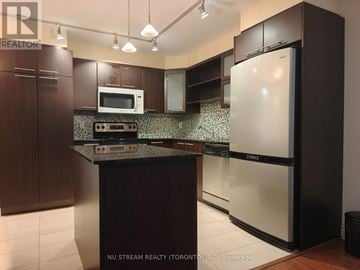 Markham (Commerce Valley) condo for rent - A kitchen with a white fridge and a black counter top.