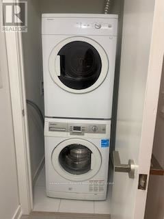 Toronto (Waterfront Communities) condo for rent - A white front loading washing machine with a dryer on top is in a small laundry room.