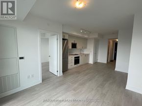 Oshawa (Windfields) condo for rent - A spacious, empty room with a kitchen area in the background.