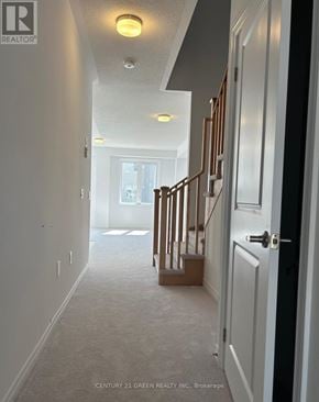 Centre Wellington (Fergus) townhouse for rent - A hallway with a carpeted floor and a staircase with wooden railings.